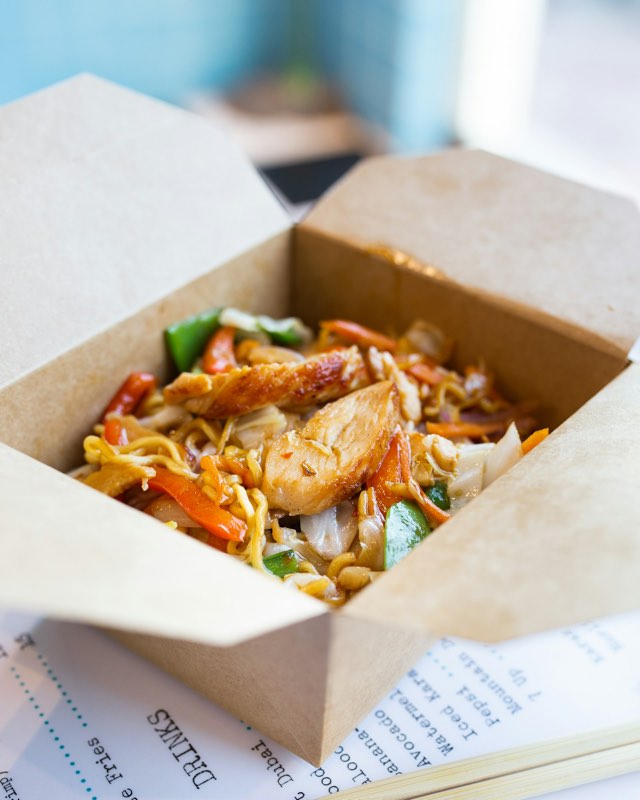 Take-out box filled with stir-fried noodles, chicken and vegetables