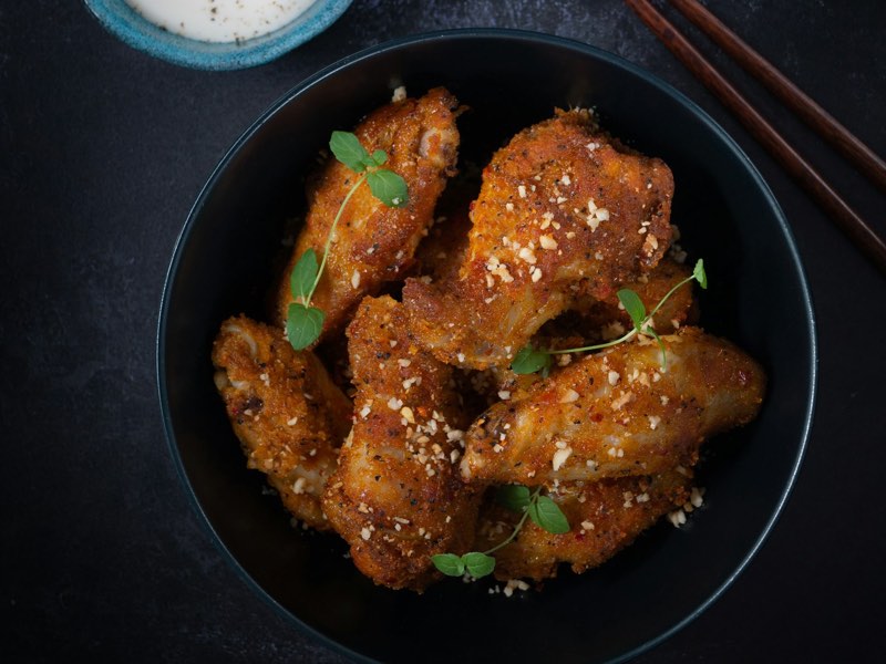 Crispy sesame chicken wings in a black bowl with chopsticks
